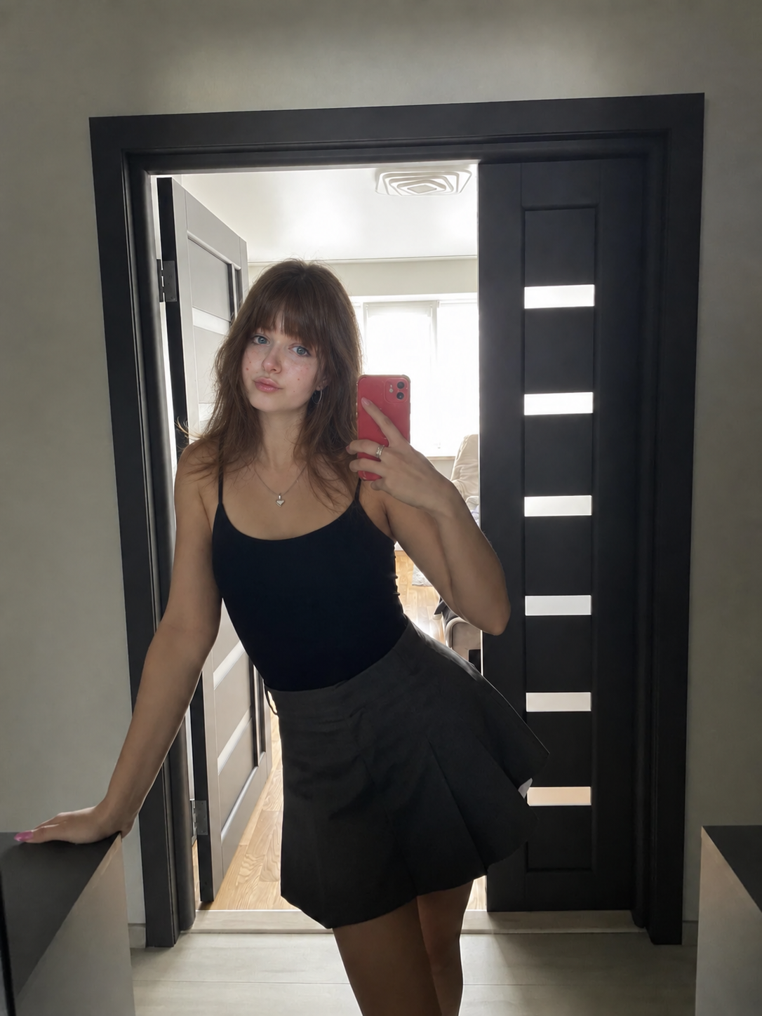 Hannah in a black top and grey skort, taking a casual mirror photo